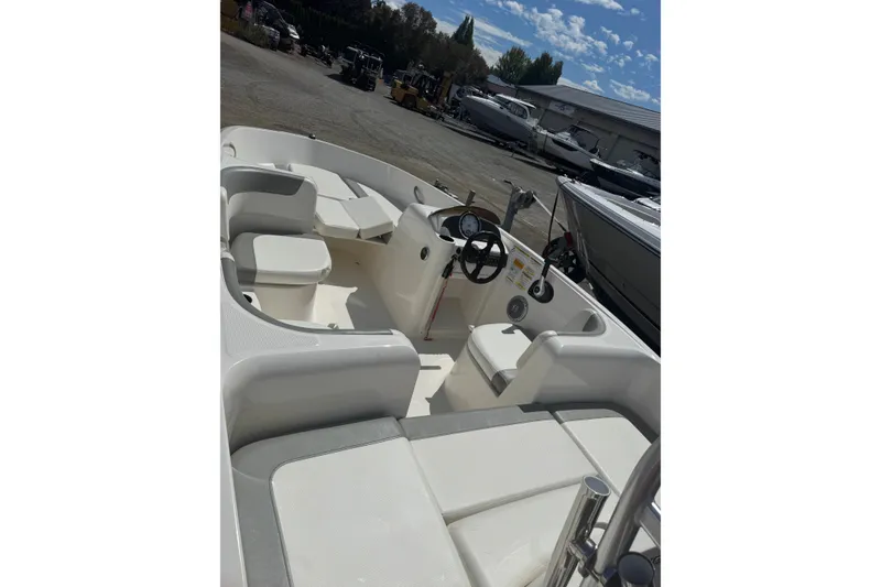 Slide: The Image of 2014 Bayliner 160 Element boat interior with seating and steering wheel, parked outdoors. - 2