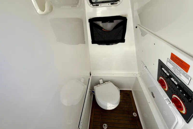 Slide: The Image of The image shows a clean, white boat toilet with a wooden floor and a black mesh pocket. - 17