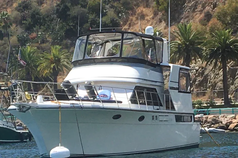 Slide: The Image of 1990 Californian 48 Motor Yacht anchored near palm trees and rocky shoreline. - 1