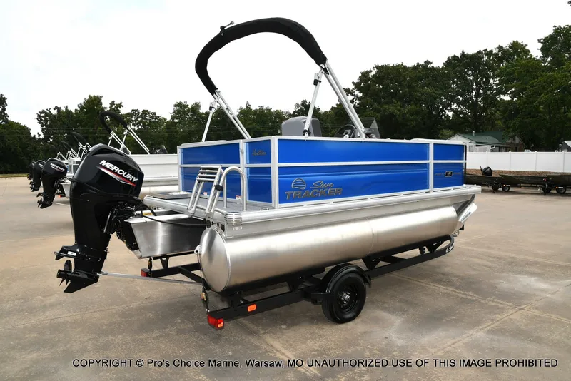 Slide: The Image of A 2027 Sun Tracker Party Barge 16 on a trailer. It features a blue hull and a Mercury outboard motor. - 14