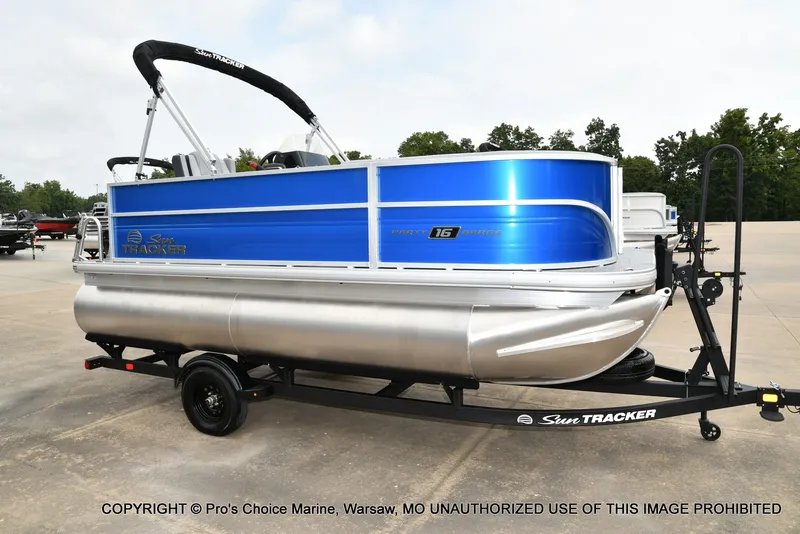 The Image of A 2027 Sun Tracker Party Barge 16 on a trailer, featuring a blue hull and silver pontoons. - 1