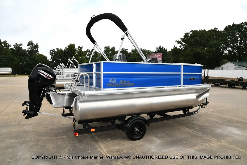 Slide: The Image of A 2027 Sun Tracker Party Barge 16 pontoon boat on a trailer, featuring a blue structure and black motor. - 15