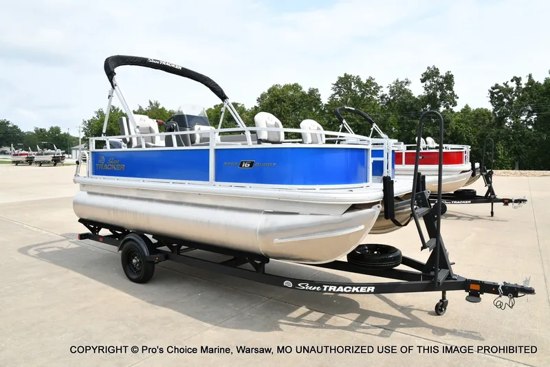 Slide: The Image of A blue and white pontoon boat on a trailer, surrounded by trees and a clear sky. - 15