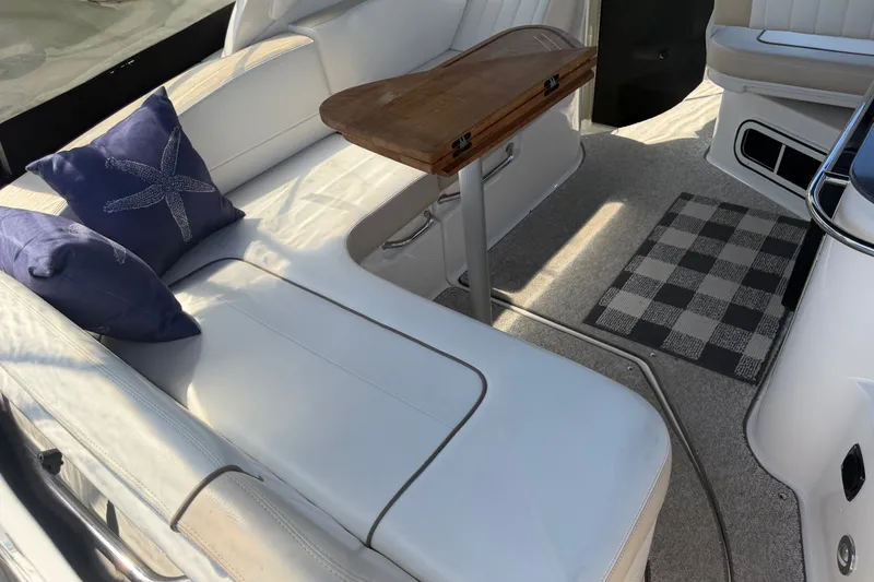 Slide: The Image of Interior of 2013 Sea Ray Sundancer 280 with white seating, wooden table, and decorative pillows. - 4