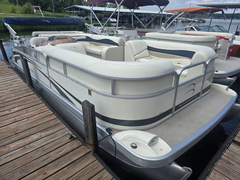 Slide: The Image of A 2008 Bennington 2050GL pontoon boat docked at a wooden pier. It features cream-colored seating. - 2