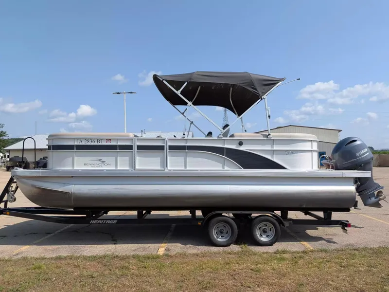 The Image of A silver 2019 Bennington pontoon boat on a trailer under a blue sky. - 1
