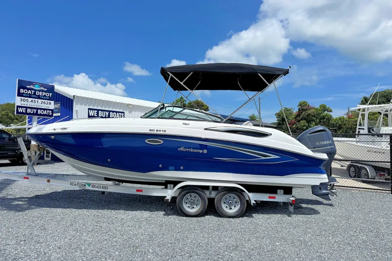 The Image of 2023 Hurricane SunDeck 2410 OB boat on trailer at dealership under blue sky. - 1