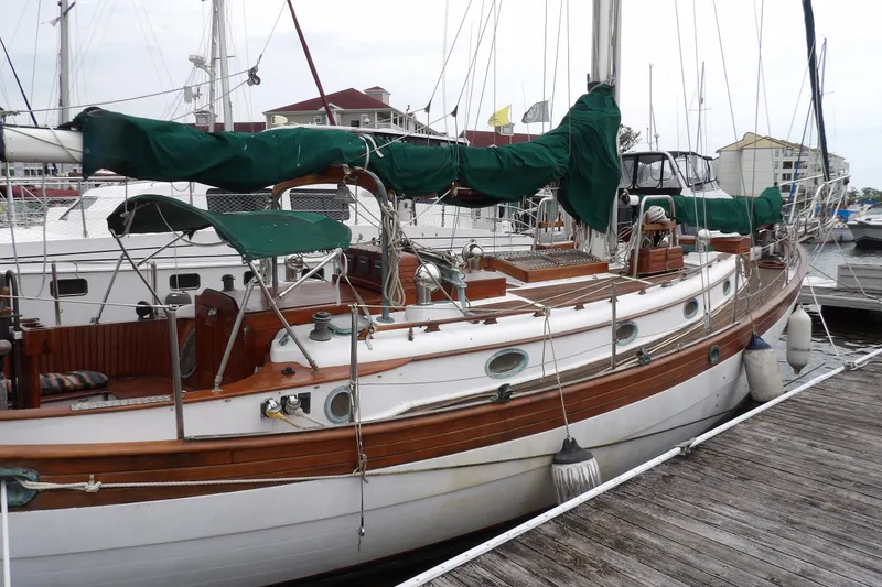 Slide: The Image of 1986 Hans Christian 43 T sailboat docked, featuring classic wooden design and green sail covers. - 6