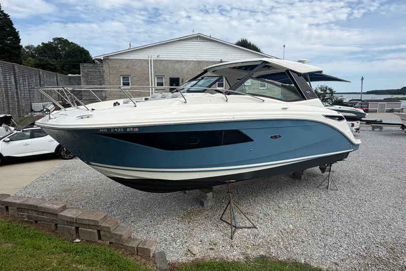 Slide: The Image of 2021 Sea Ray Sundancer 320 boat displayed on gravel lot, blue and white exterior. - 2