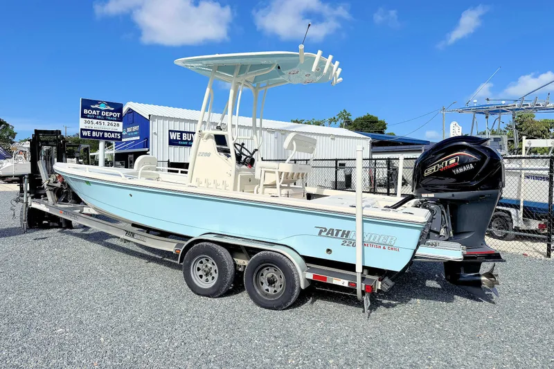 The Image of A 2023 Pathfinder 2200 TRS boat on a trailer, featuring a Yamaha outboard motor, in front of a boat depot. - 1