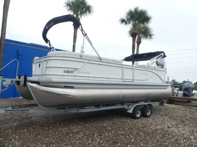 Slide: The Image of A 2024 Sweetwater SW 2286 SB pontoon boat on a trailer, surrounded by palm trees. - 2