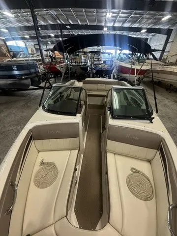 Slide: The Image of A 2013 Sea Ray SLX 230 boat in a warehouse. It features beige upholstery and a black canopy. - 17
