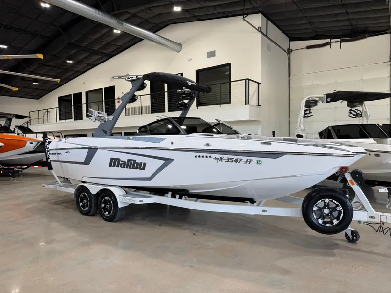 The Image of A white 2021 Malibu Wakesetter 24 MXZ boat on a trailer inside a showroom. - 1