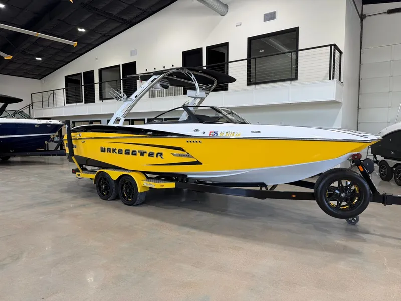The Image of A yellow 2014 Malibu Wakesetter 24 MXZ boat on a trailer in a showroom. - 1