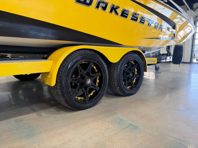Slide: The Image of A yellow 2014 Malibu Wakesetter 24 MXZ on a trailer with black wheels. - 5