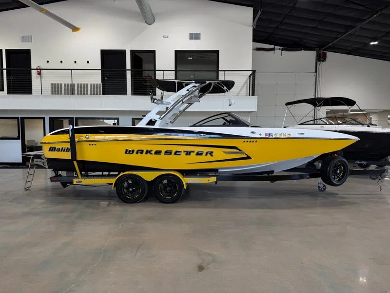 Slide: The Image of 2014 Malibu Wakesetter 24 MXZ in bright yellow, on a trailer inside a showroom. - 2