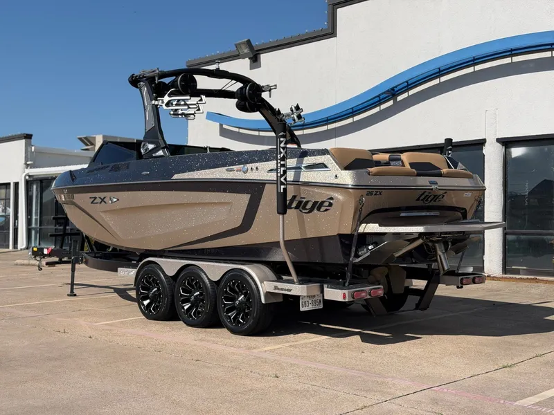 Slide: The Image of A 2022 Tigé 25ZX boat on a trailer, parked on a concrete lot in front of a building. - 3