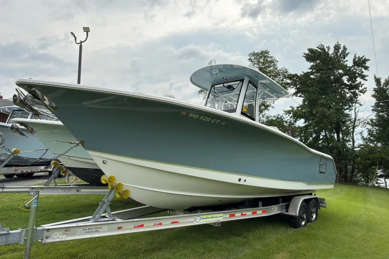 Slide: The Image of 2019 Sea Hunt Gamefish 27 boat on trailer, parked on grass under cloudy sky. - 1