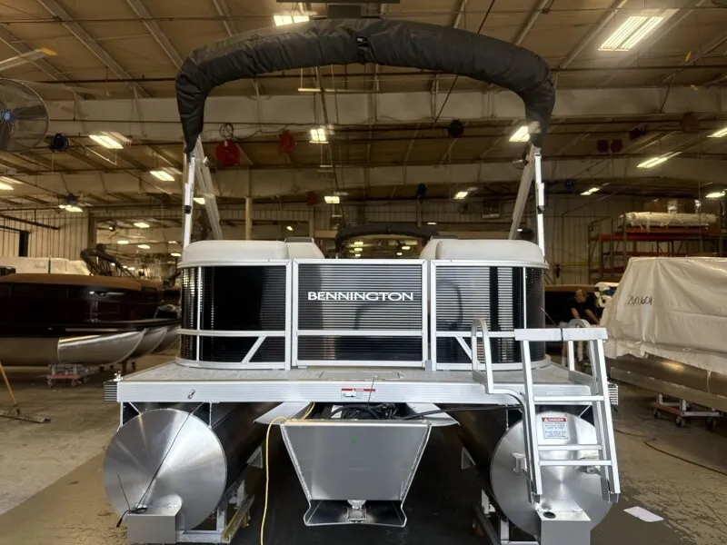 The Image of Bennington 20 S1 STERN RADIUS pontoon boat in a warehouse with a Bimini top and aluminum hull. - 1