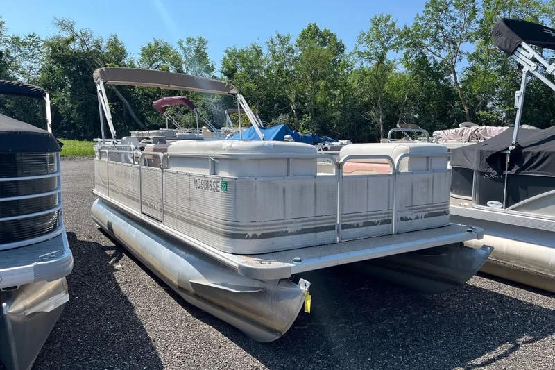 The Image of 2001 SMOKERCRAFT pontoon boat parked on gravel, surrounded by trees and other boats. - 1