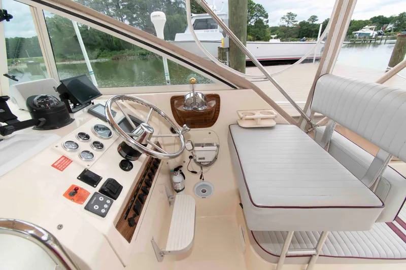 Slide: The Image of 2001 Mainship Pilot 30 helm with steering wheel, gauges, and seating, docked by a serene waterfront. - 10