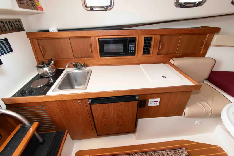 Slide: The Image of 2001 Mainship Pilot 30 galley with stove, sink, microwave, and wooden cabinetry. - 18