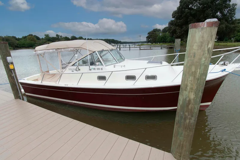 The Image of 2001 Mainship Pilot 30 docked by a serene river under a cloudy sky. - 0