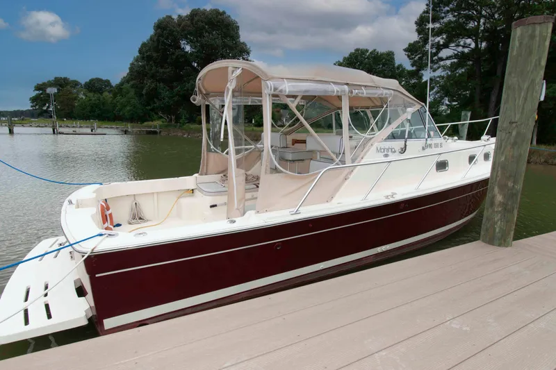 Slide: The Image of 2001 Mainship Pilot 30 docked, featuring a maroon hull and beige canopy, surrounded by serene water. - 3