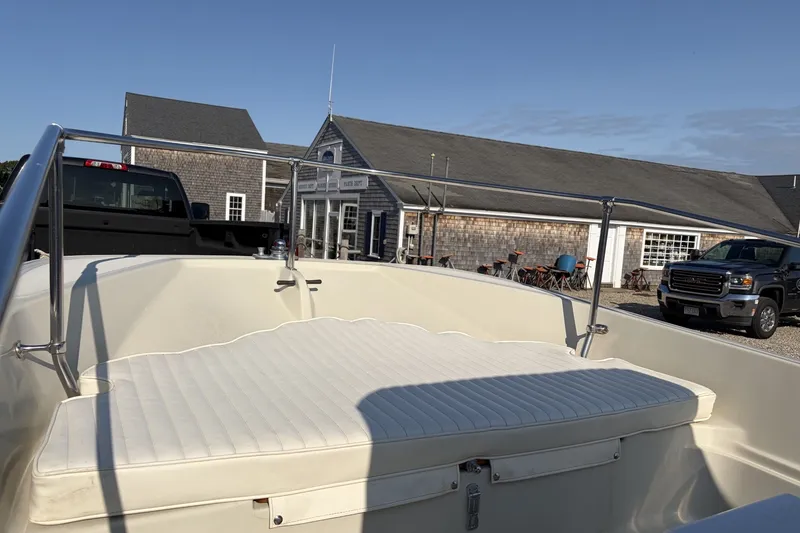 Slide: The Image of 1985 Boston Whaler 17 Montauk boat interior with cushioned seating, parked near rustic buildings. - 20