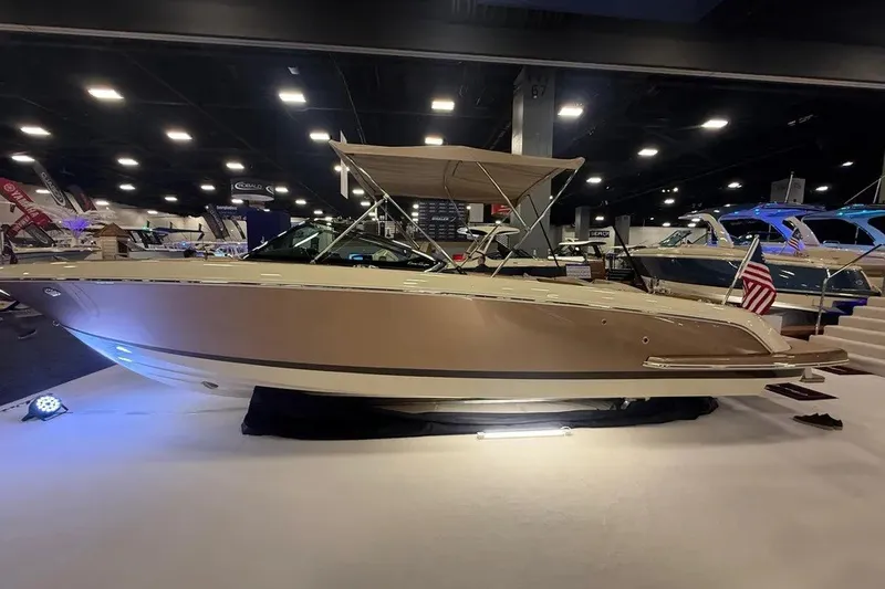 The Image of 2026 Chris-Craft Launch 27 boat displayed indoors with canopy and American flag. - 1