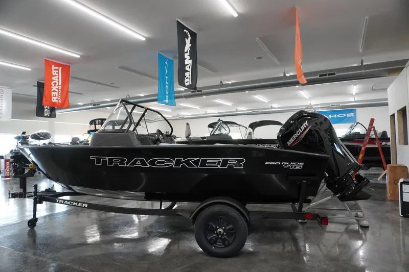 The Image of 2027 Tracker Pro Guide V-16 WT boat displayed in showroom with banners overhead. - 1