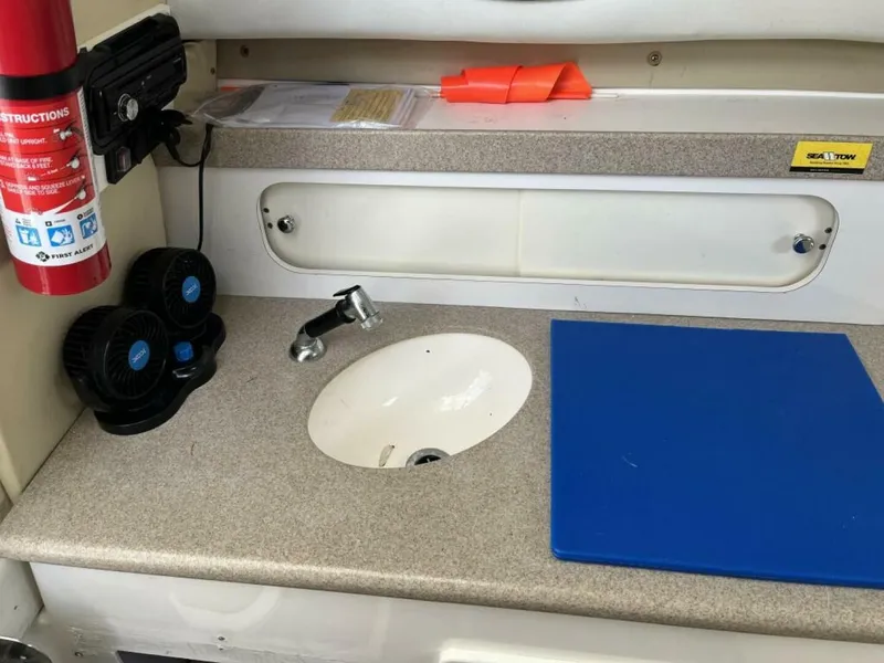 Slide: The Image of A boat's kitchenette with a sink, fire extinguisher, and blue cutting mat. - 10