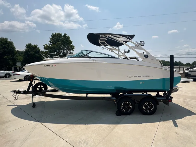 Slide: The Image of 2020 Regal LS4 Surf on a trailer, turquoise hull, black canopy, parked outdoors. - 2
