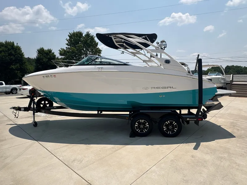 Slide: The Image of 2020 Regal LS4 Surf boat with turquoise hull on a trailer, parked outdoors. - 6