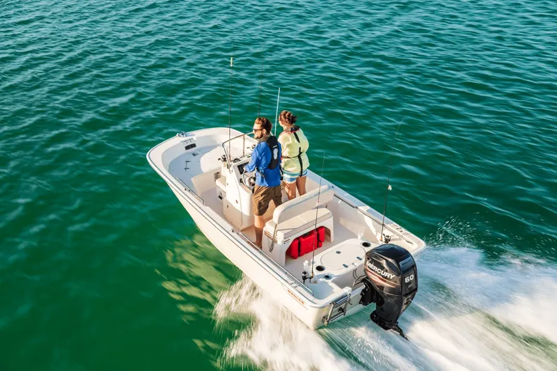 Slide: The Image of A 2027 Boston Whaler 150 Montauk cruising on calm waters. Two people are standing on board. - 17