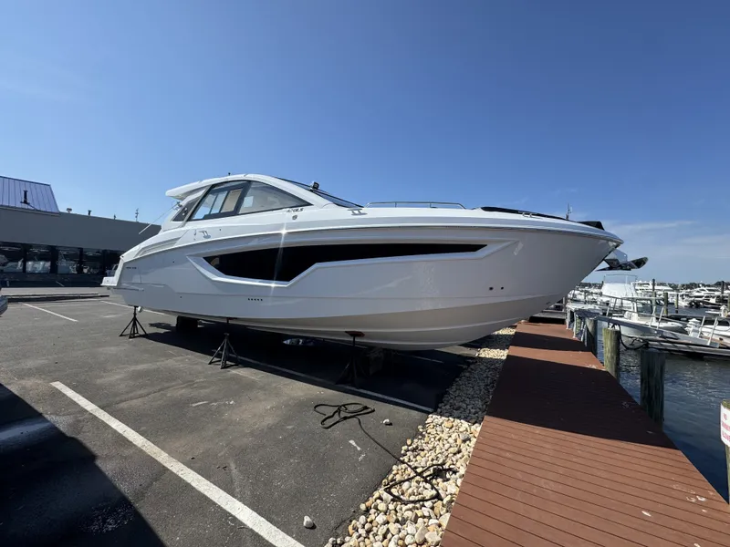 Slide: The Image of A modern 2027 Cruisers Yachts 42 GLS OB is parked near a marina on a paved lot. - 1