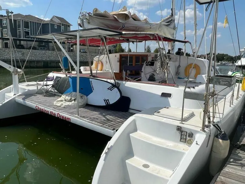 Slide: The Image of A 1995 Voyage Yachts Mayotte catamaran docked. It features a spacious deck with a surfboard. - 5