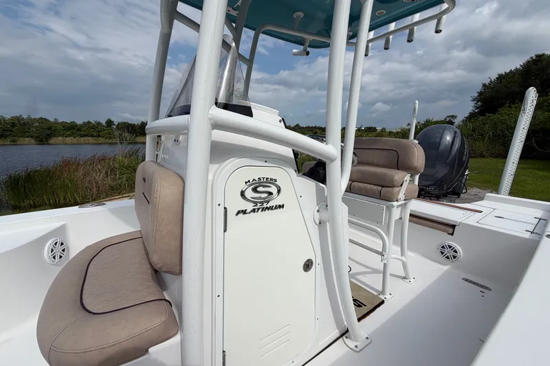 Slide: The Image of 2019 Sportsman Masters 227 Bay Boat interior with seating and console, near a serene lake. - 13