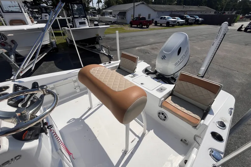 Slide: The Image of 2025 NauticStar 191 Hybrid boat interior with seating and steering wheel, parked outdoors. - 13
