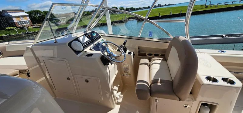 Slide: The Image of 2014 Grady-White Freedom 285 boat interior with steering wheel and seating, docked by a scenic waterfront. - 14