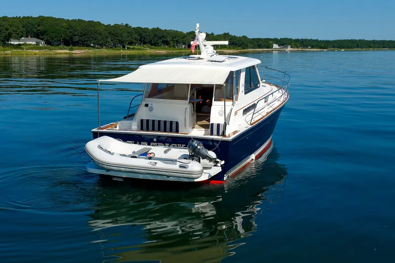 Slide: The Image of 2006 Sabre 42 Hard Top Express yacht on calm water, featuring a small dinghy. - 60