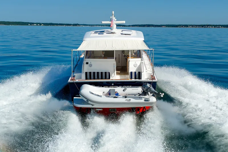 Slide: The Image of 2006 Sabre 42 Hard Top Express cruising on open water, rear view with dinghy attached. - 61