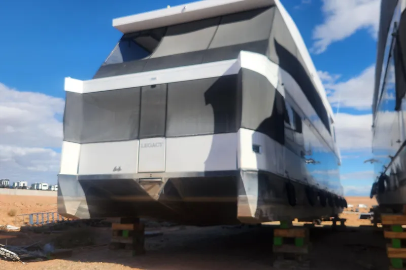 Slide: The Image of Modern Adonia Legacy Trip #15 houseboat elevated on blocks, 2022 model, under a clear blue sky. - 2