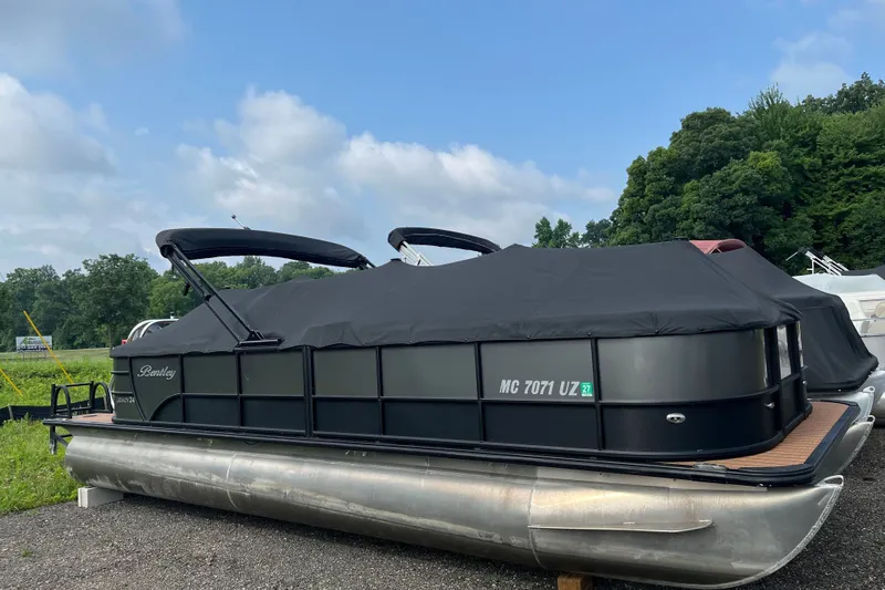Slide: The Image of 2024 Bentley Pontoons Legacy 240 Navigator, covered, parked outdoors with lush greenery. - 2