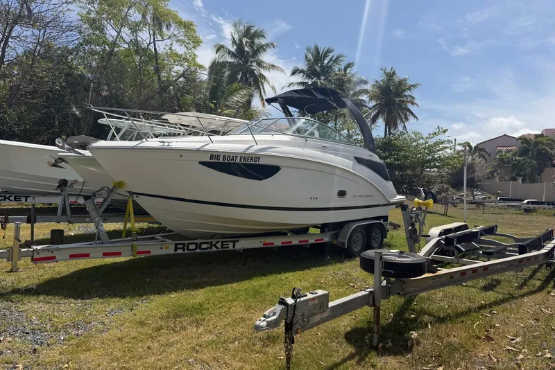 Slide: The Image of 2022 Regal 26 XO boat on trailer, parked outdoors with palm trees in background. - 6