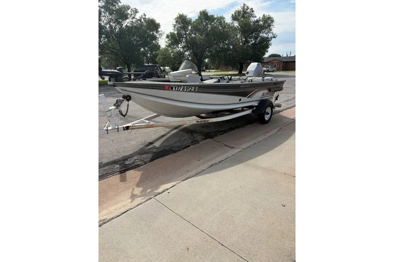 Slide: The Image of 1998 Alumacraft boat on trailer parked on a street, surrounded by trees. - 6