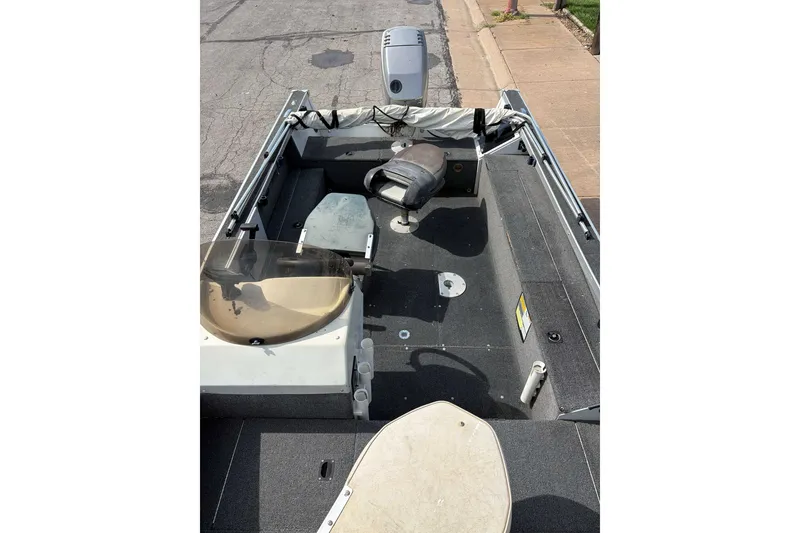 The Image of 1998 Alumacraft boat interior with seating and steering console, parked on pavement. - 1