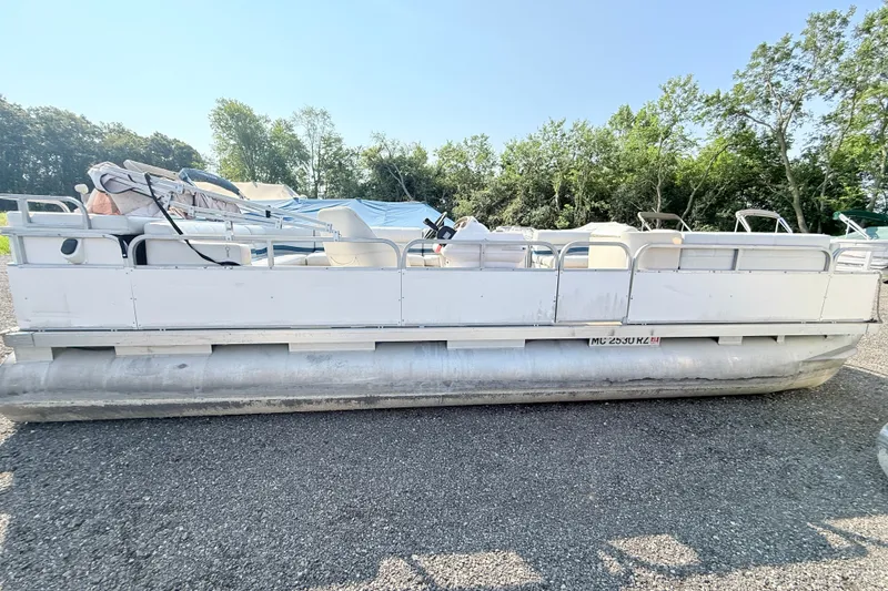 The Image of 1999 Crest 240 pontoon boat on gravel lot, surrounded by trees. - 0