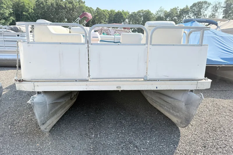 Slide: The Image of 1999 Crest 240 pontoon boat on gravel lot, surrounded by trees and other boats. - 1
