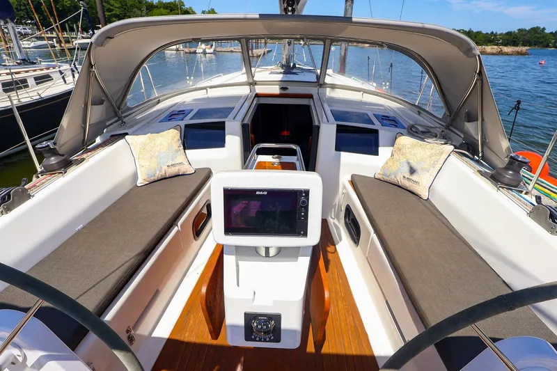 Slide: The Image of 2016 Hanse 385 sailboat cockpit with navigation system, cushions, and canopy in marina setting. - 53